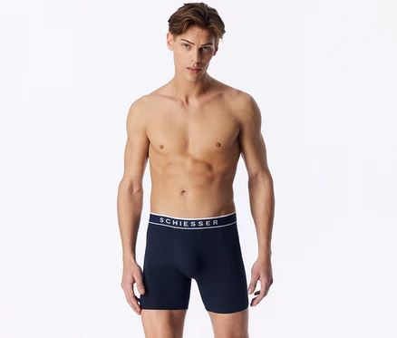 Un homme torse nu porte un boxer bleu foncé avec une ceinture blanche SCHIESSER.