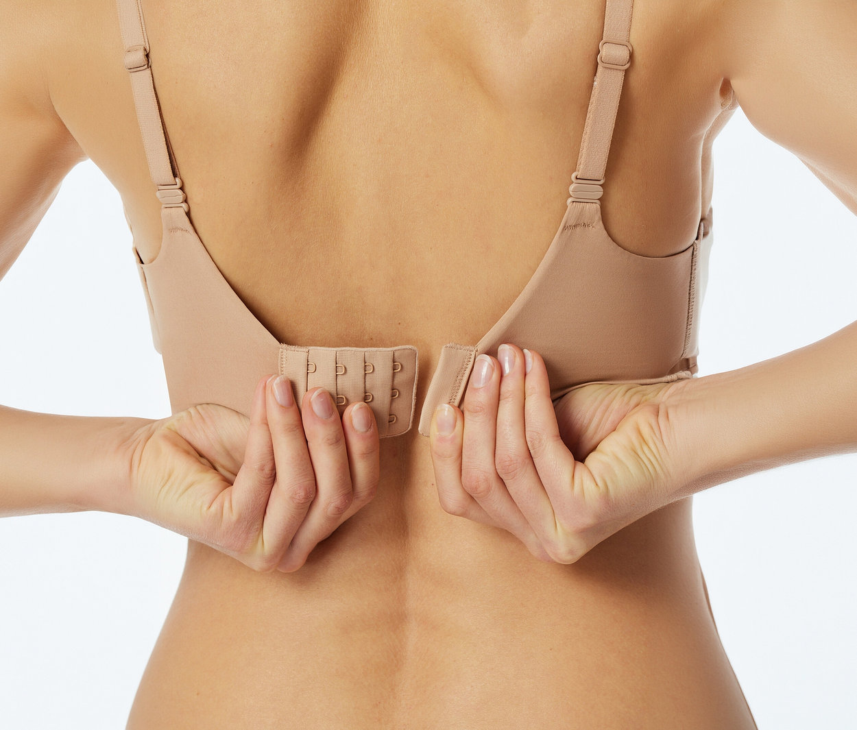 Deux mains attachent un soutien-gorge beige dans le dos d'une personne, montrant la fermeture à quatre agrafes.