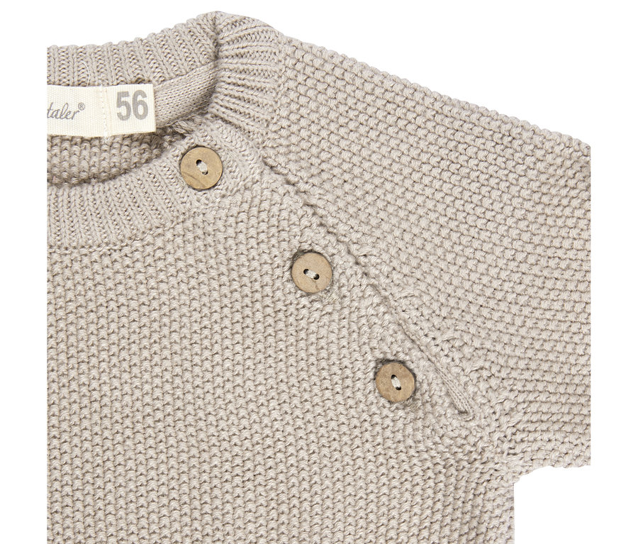 Gros plan d'un pull en tricot beige avec trois boutons ronds en bois sur l'épaule et une étiquette de taille 56.