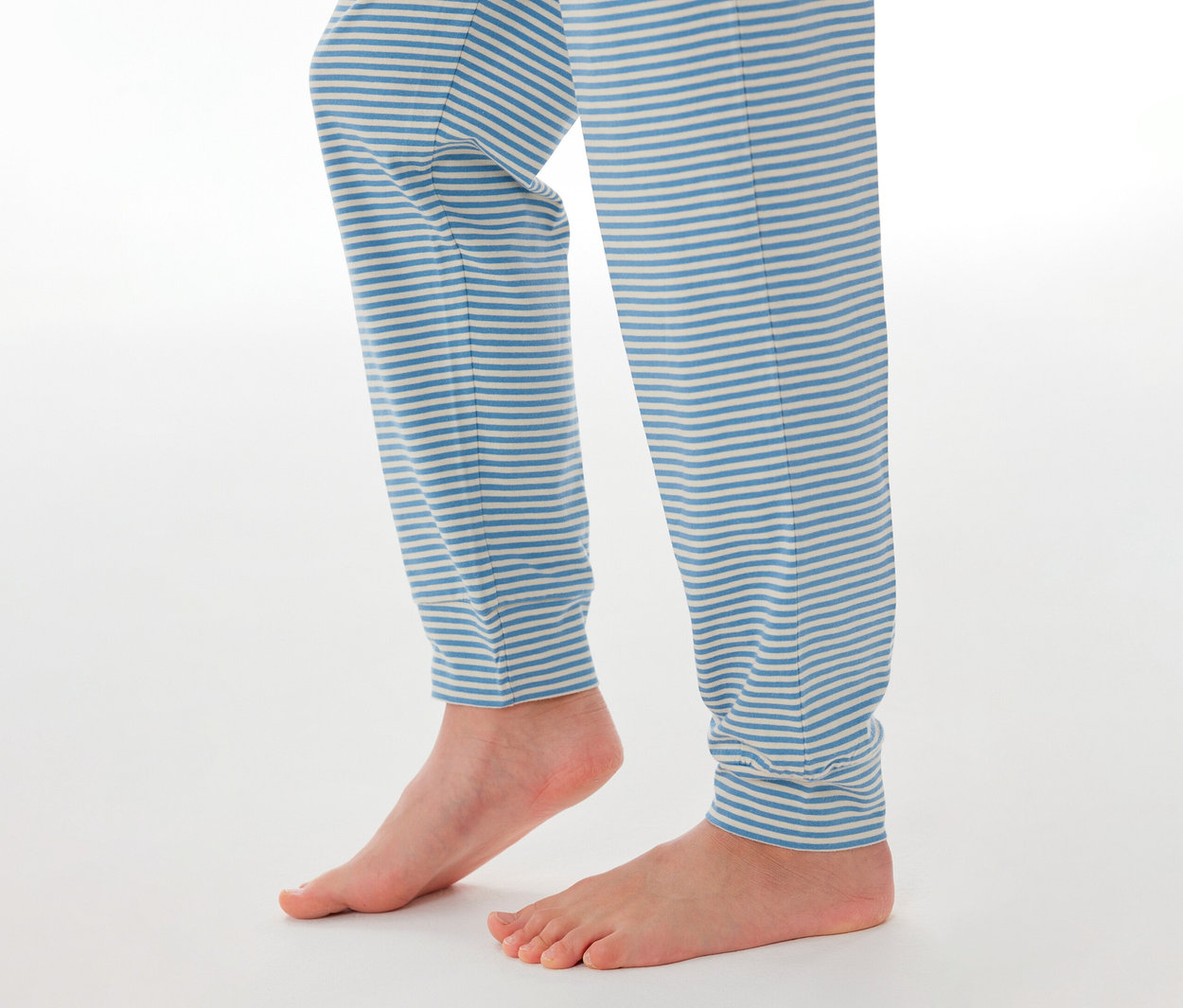 Jambes et pieds nus d'un enfant portant un bas de pyjama enfant SCHIESSER à rayures bleues et blanches.