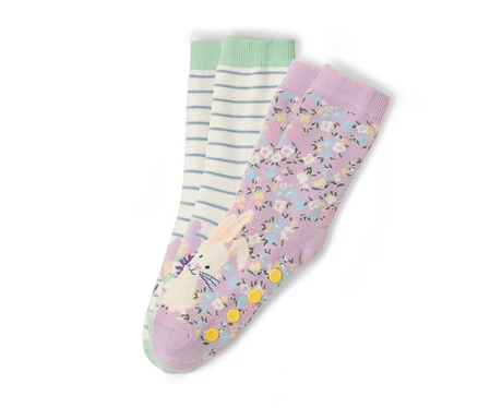 Trois paires de chaussettes sont posées sur un fond blanc. Une paire est violette avec un motif floral et un imprimé de lapin. Une paire est blanche avec des rayures bleues et une bordure verte.