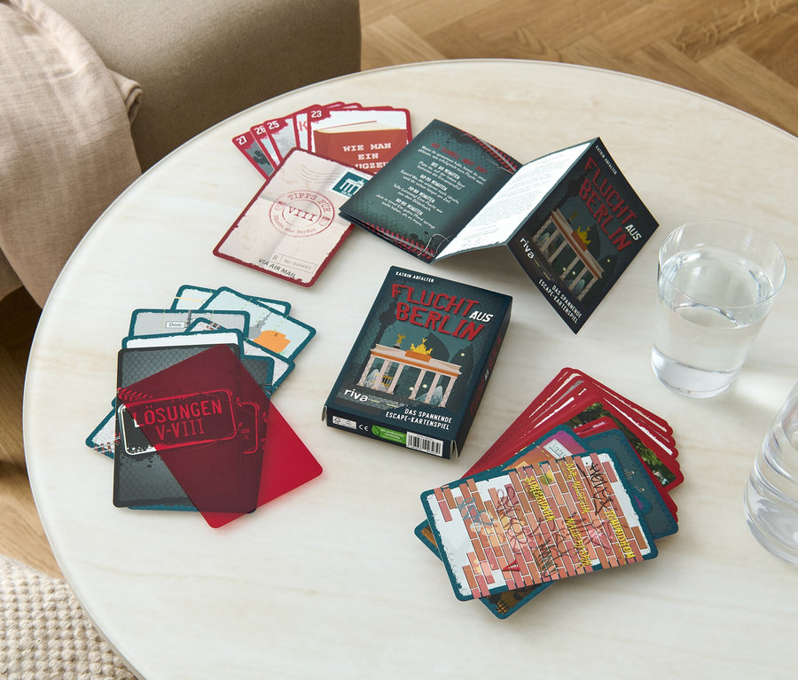Sur une table se trouvent un jeu de cartes Escape Game « Flucht aus Berlin » (Sortir de Berlin, en allemand), un verre d'eau et une carafe.