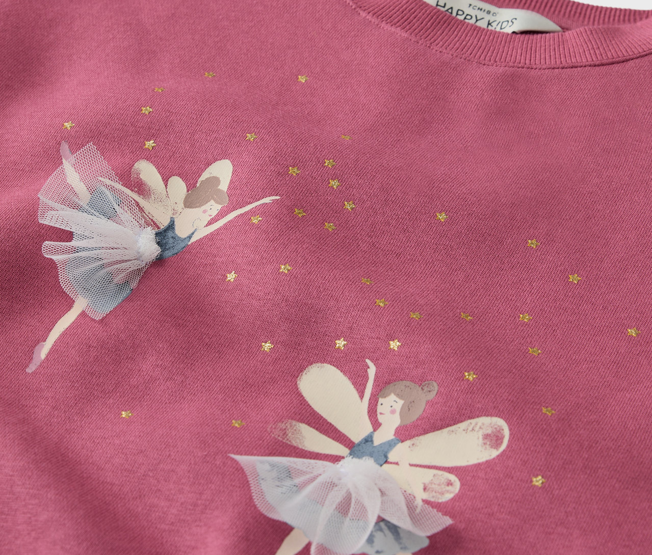 Gros plan sur un sweat-shirt rose orné de deux fées et d'étoiles dorées.