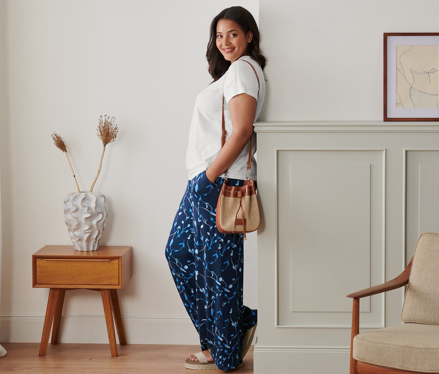 Une femme appuyée contre un mur pose en pantalon palazzo, t-shirt blanc et sandales à plateau en cuir. Un sac à main est porté à l'épaule.