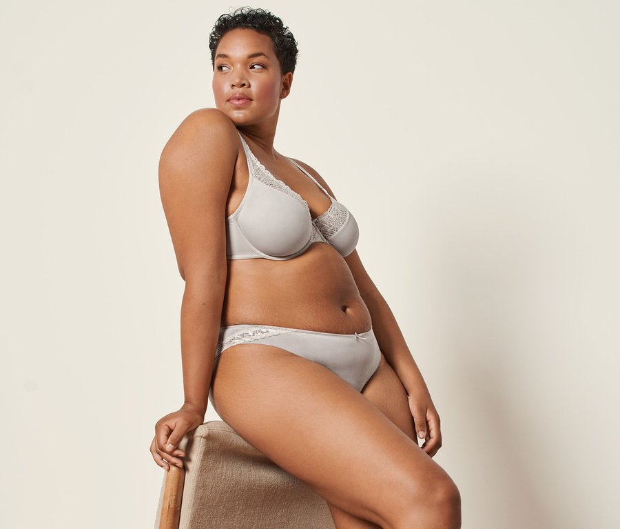 Une femme est assise sur une chaise et porte 2 culottes grège et un soutien-gorge à armatures.