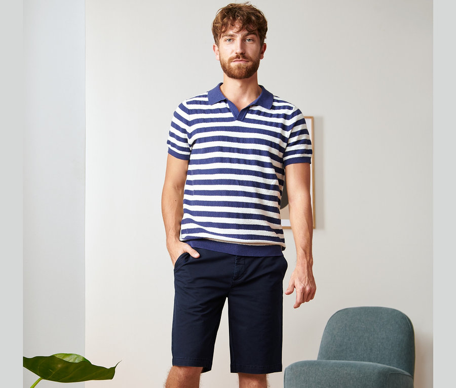 Un homme debout portant un short chino bleu marine et un polo rayé.