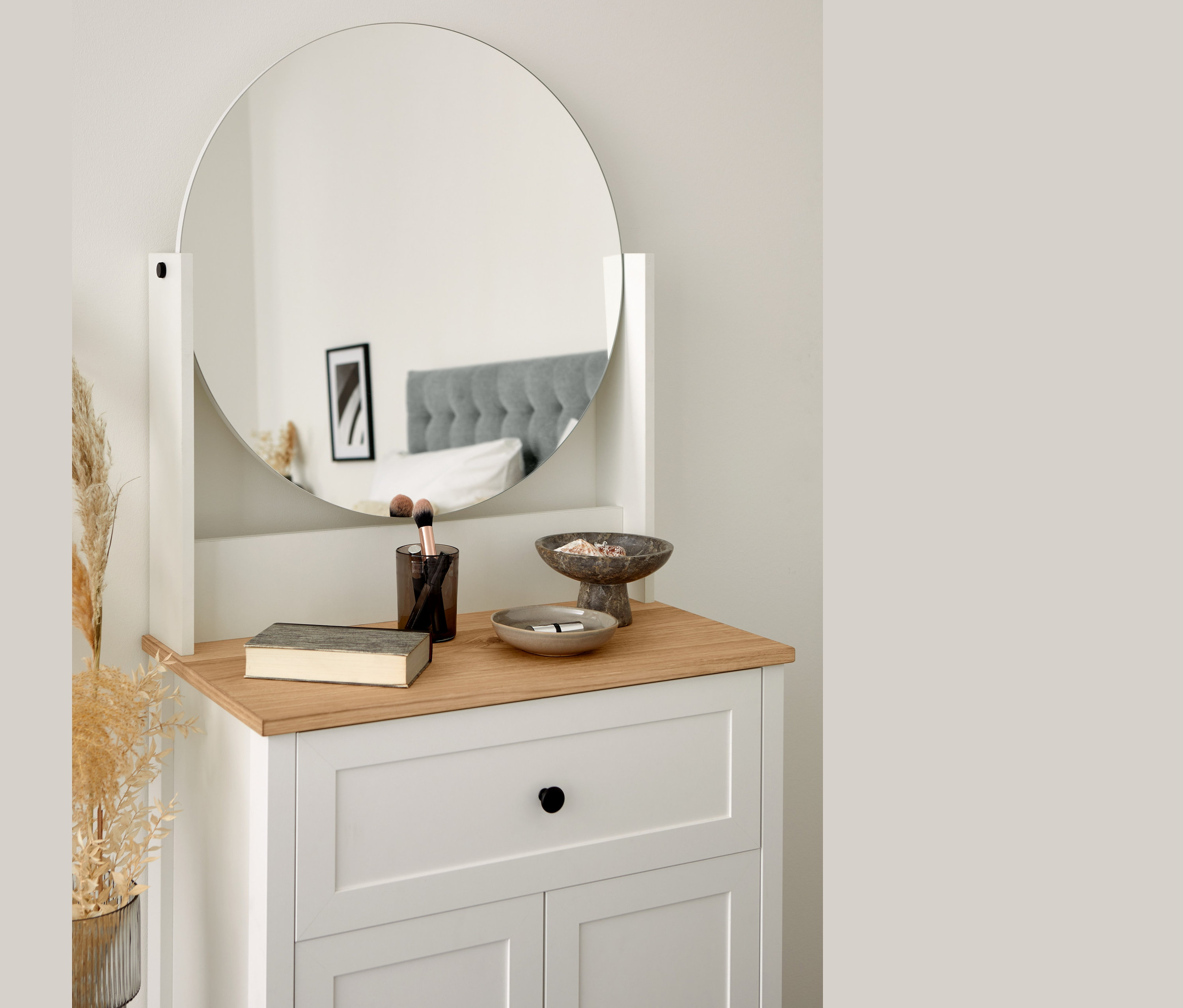 Coiffeuse « Clara » avec miroir rond, livre, pinceaux et coupelles décoratives. Un lit se reflète dans le miroir.