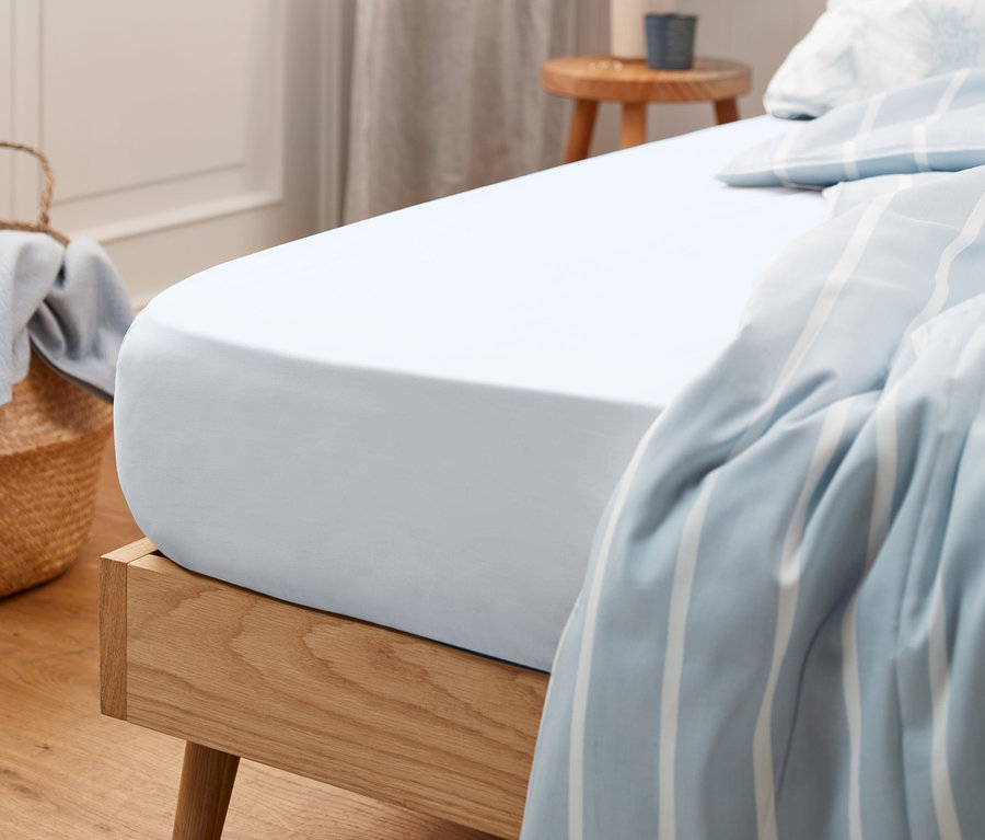 Drap-housse en jersey blanc sur un lit en bois.