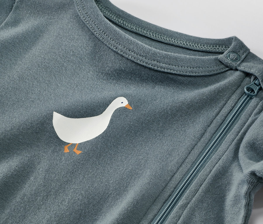 Gros plan sur un pyjama bleu pour bébé avec un motif d'oie et une fermeture éclair.