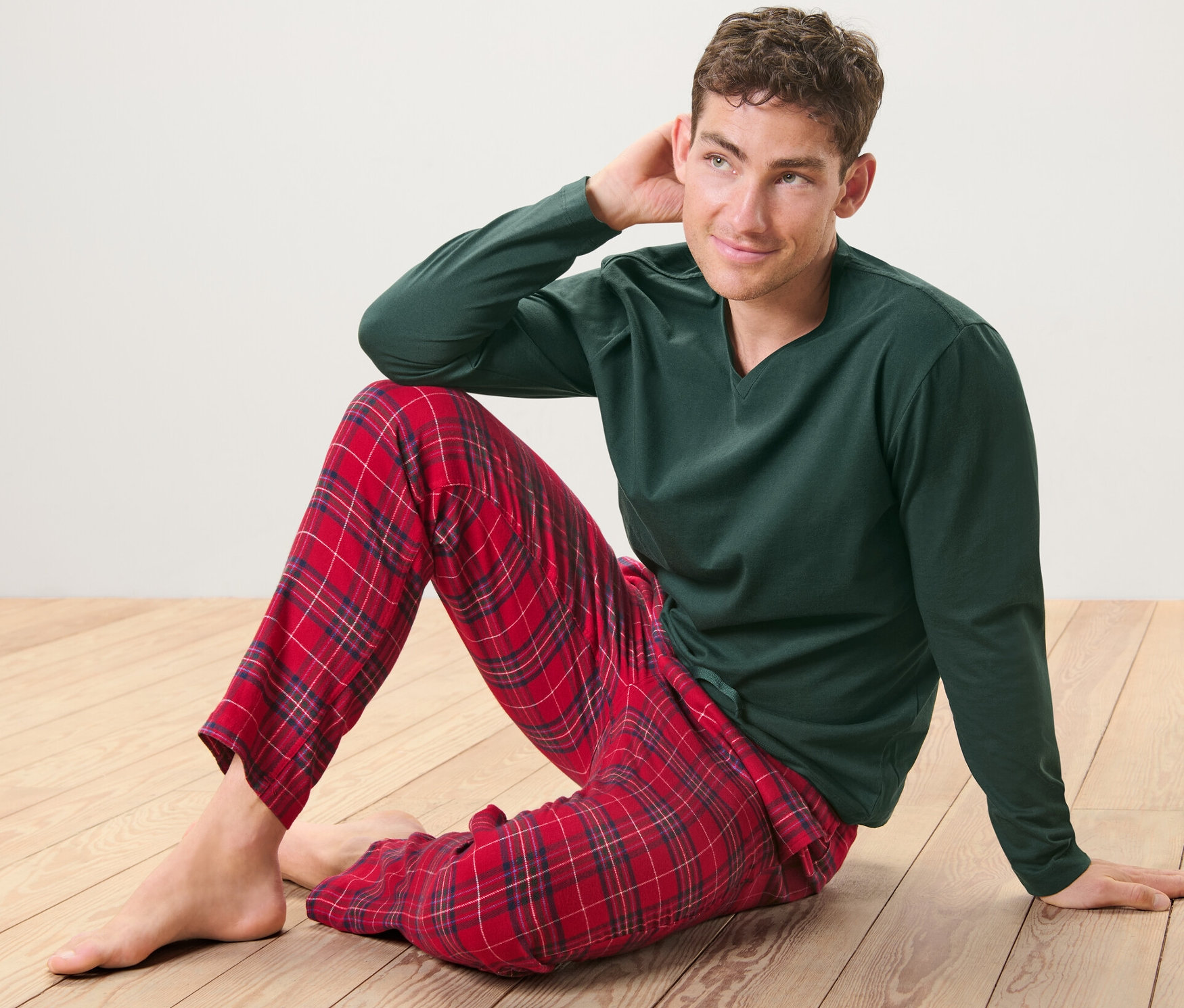 Un homme est assis sur le plancher en bois et porte un pyjama vert avec un pantalon de flanelle rouge à carreaux.