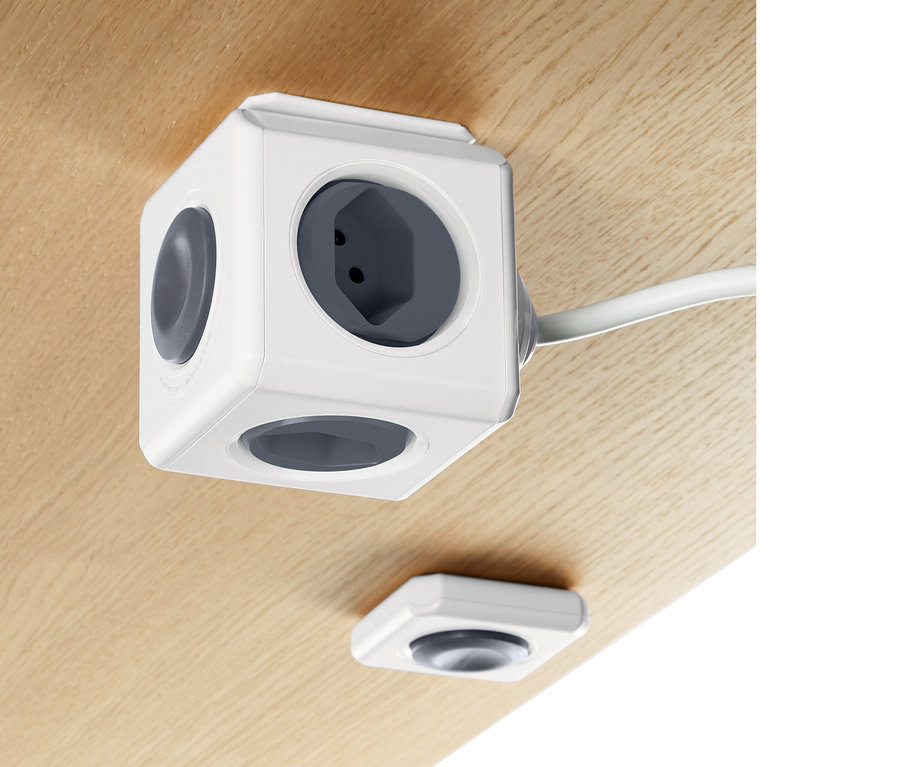 Sur une surface en bois se trouve un cube multiprise blanc avec télécommande.