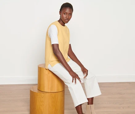 Femme assise sur des tabourets en bois portant un pull sans manches en maille.