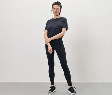 Une femme pose en t-shirt noir et legging de course à pied haute performance.
