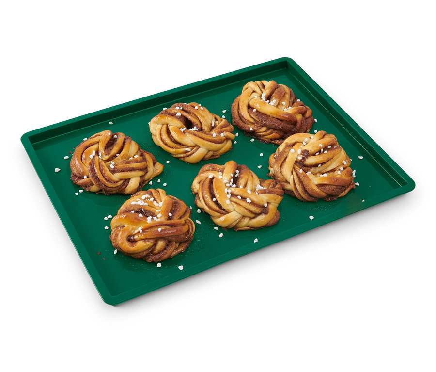 Six brioches à la cannelle sur une feuille de cuisson réutilisable verte avec bord.