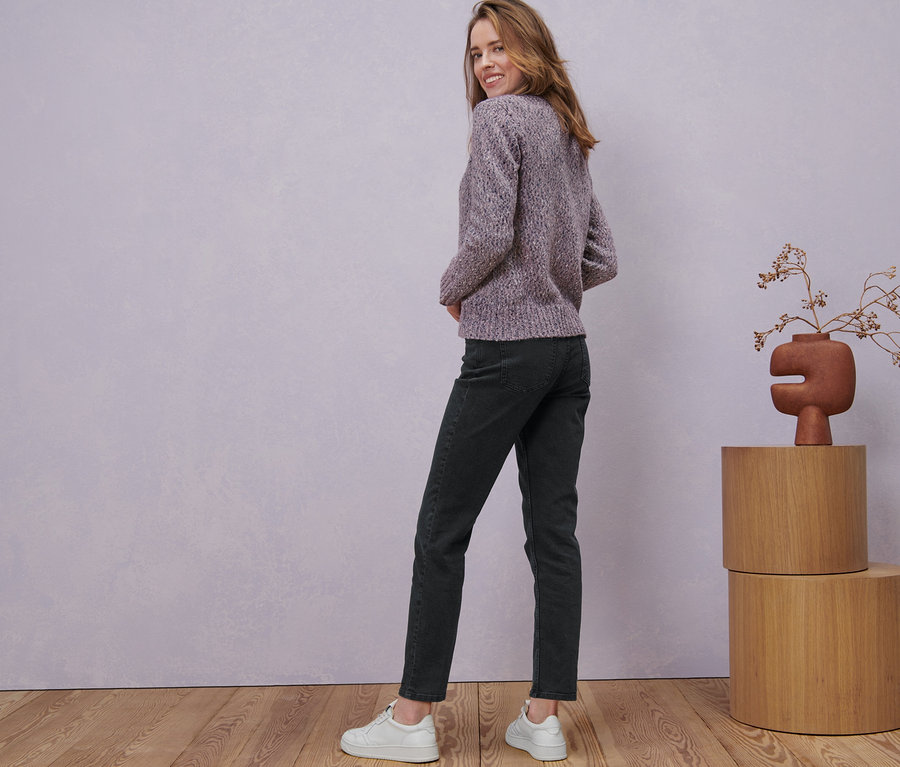 Une femme regarde par-dessus son épaule et pose en veste en maille avec de la laine, un jean et des baskets.