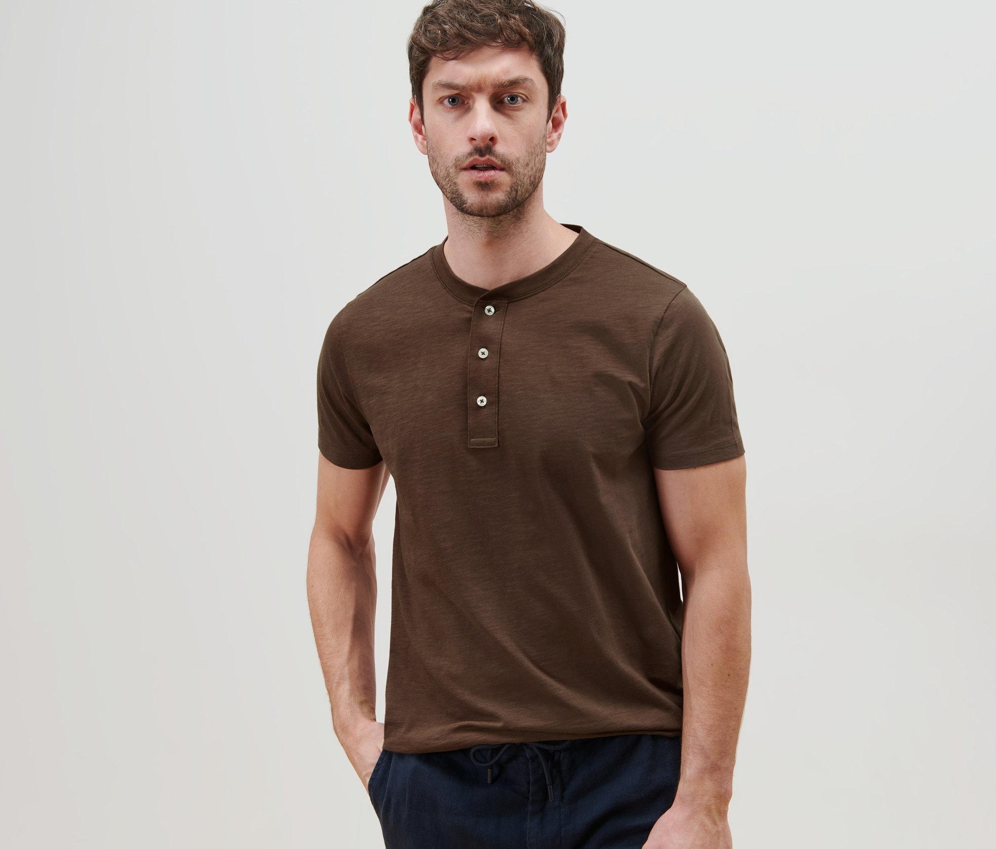 Un homme pose, portant un Henley à manches courtes marron.