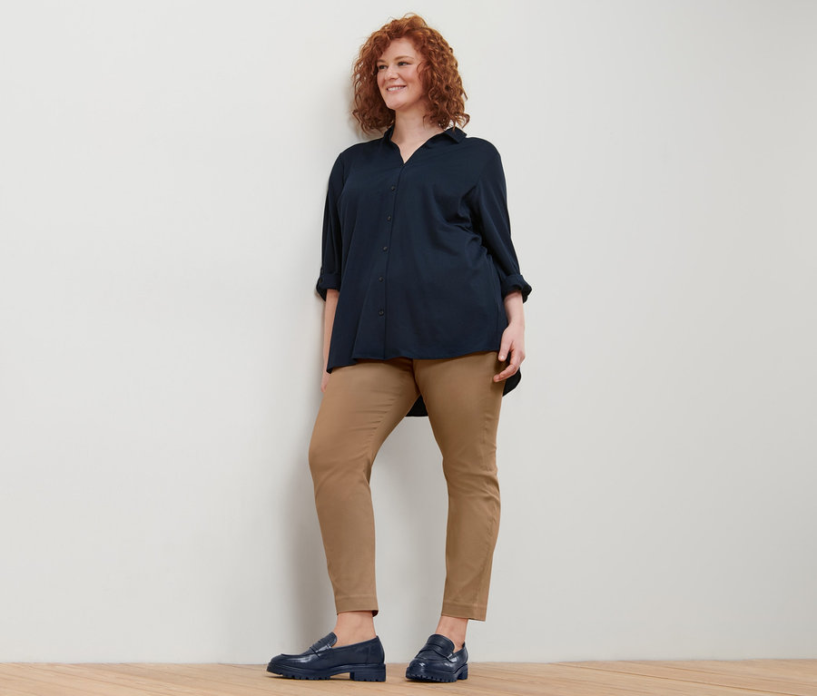 Une femme aux cheveux roux bouclés porte un chemisier en jersey piqué bleu foncé et un pantalon stretch.