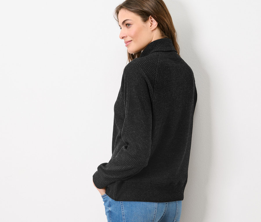 Une femme pose de profil en portant un sweatshirt camionneur et un jean.