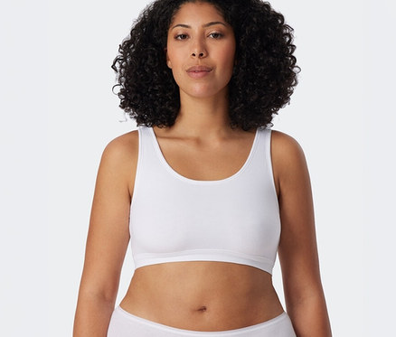 Une femme aux cheveux bouclés porte une brassière SCHIESSER blanche et une culotte blanche.