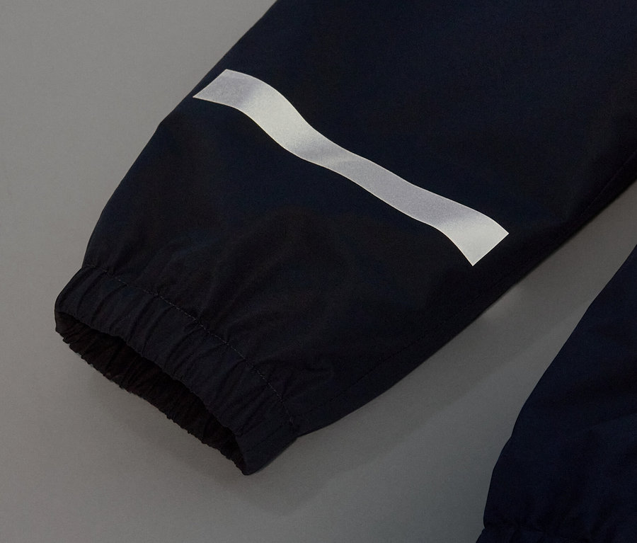 Détail d'un pantalon de pluie pour enfant bleu foncé avec une bande réfléchissante.