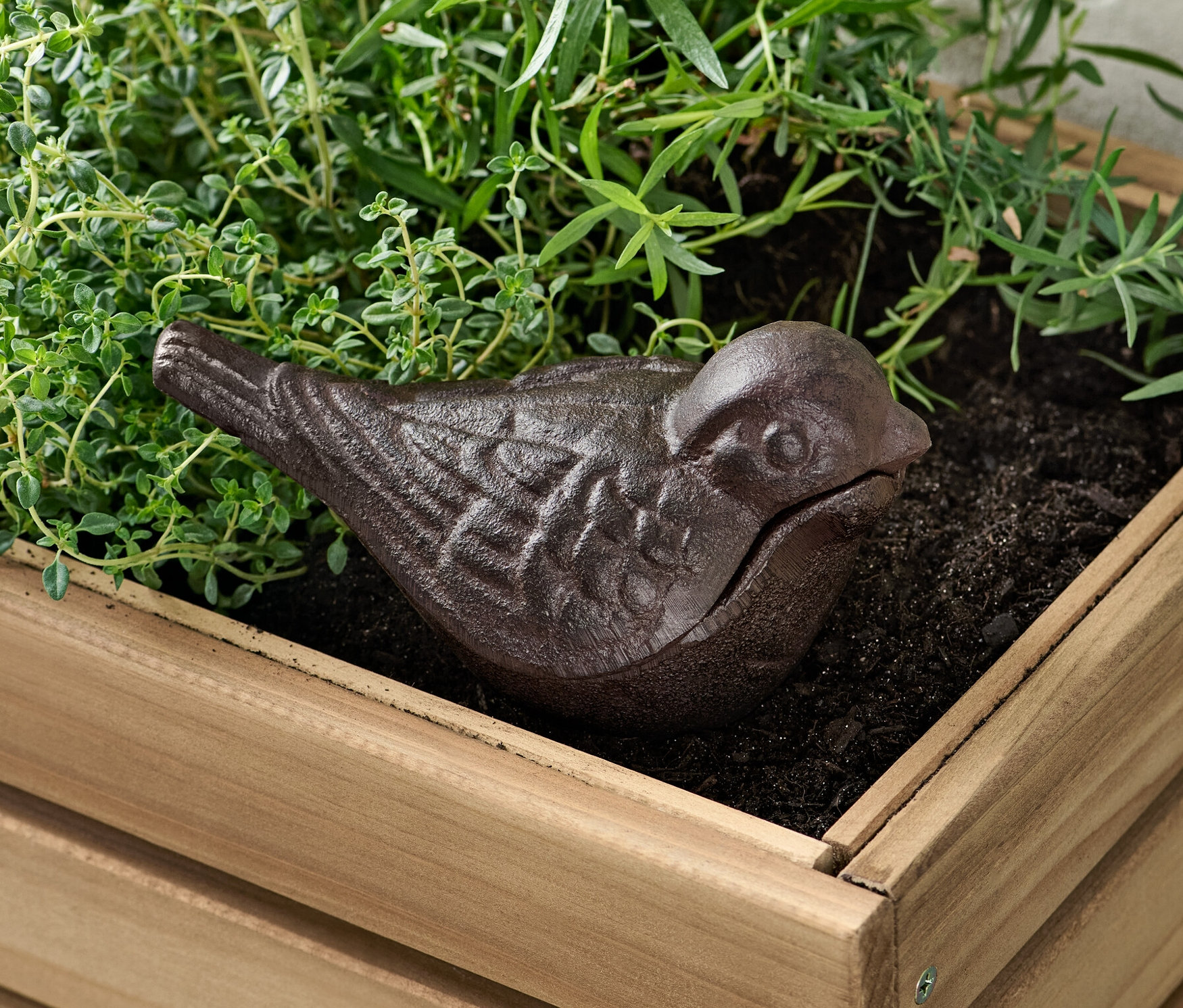 Une cachette pour clés marron en forme d'oiseau dans un pot de fleurs en bois avec des plantes.