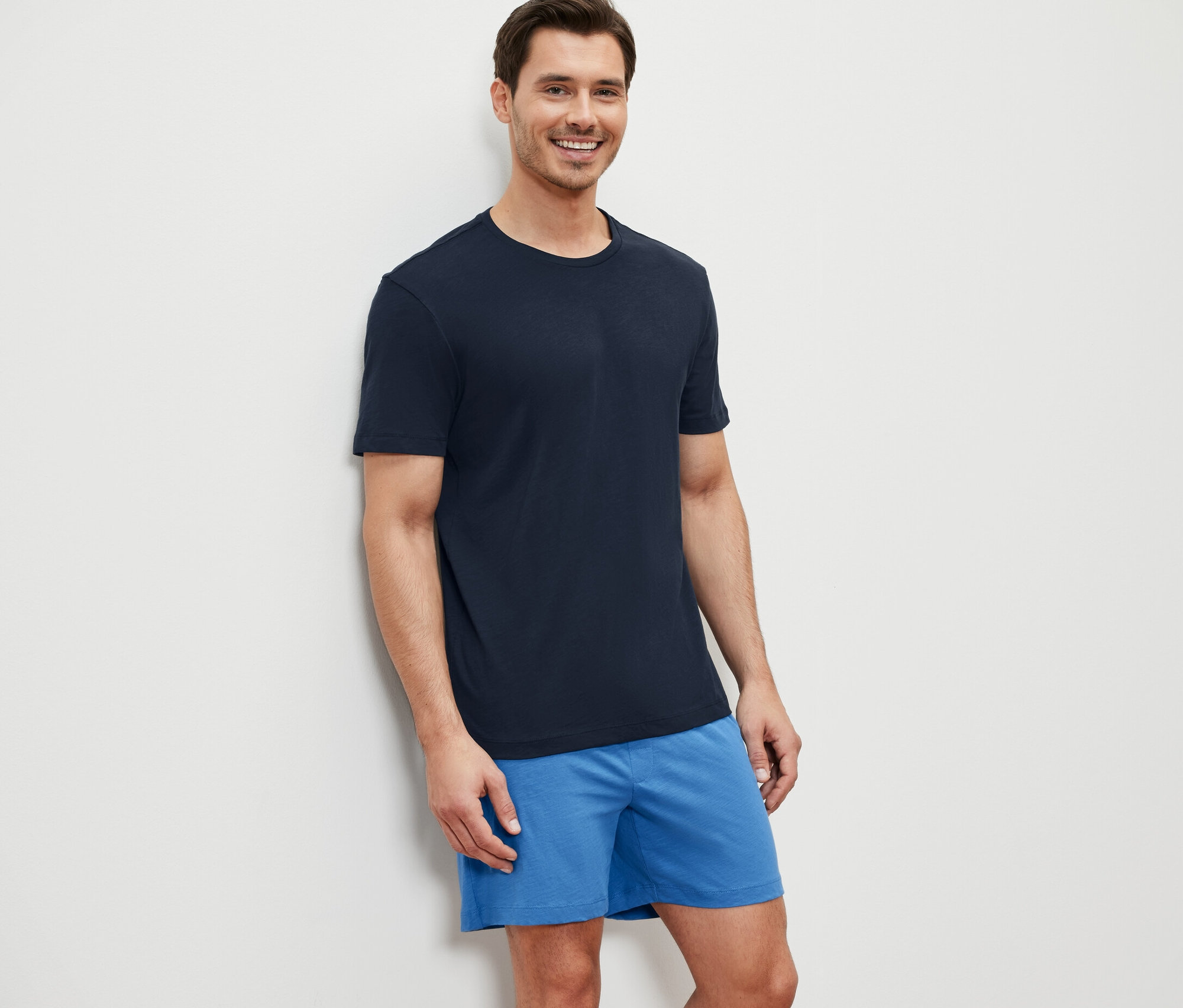 Un homme souriant, appuyé contre un mur, porte un pyjashort.