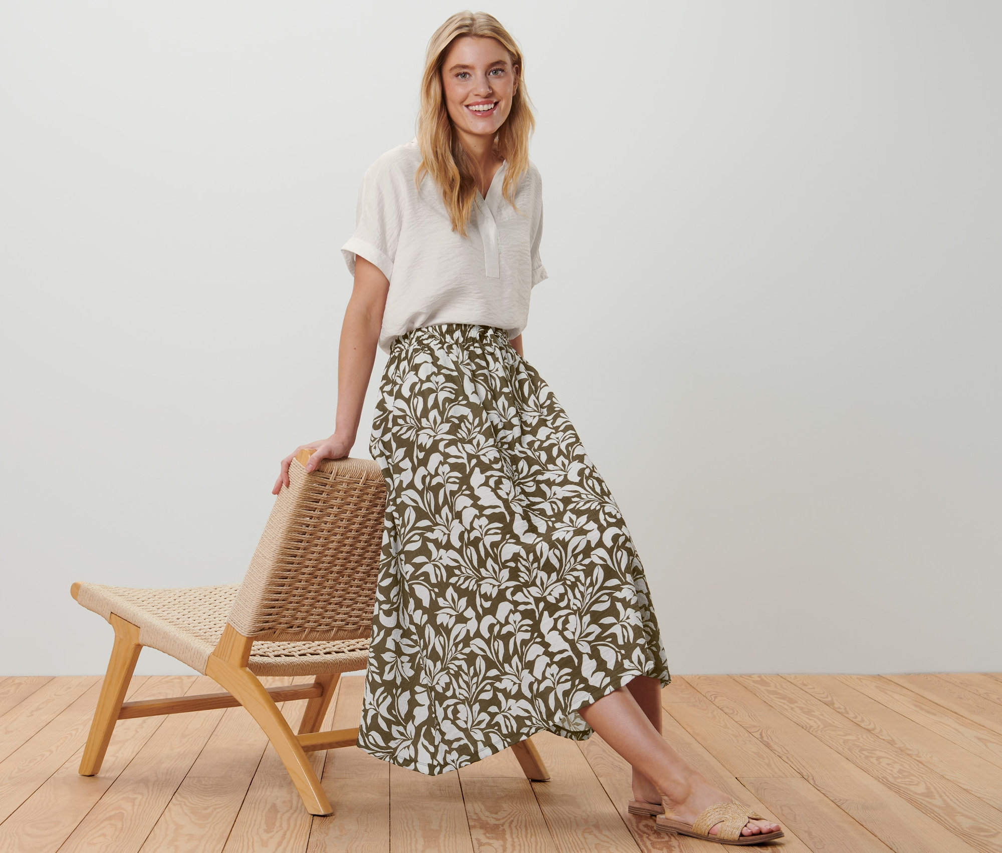 Une femme pose appuyée sur une chaise, elle porte une jupe midi imprimée.