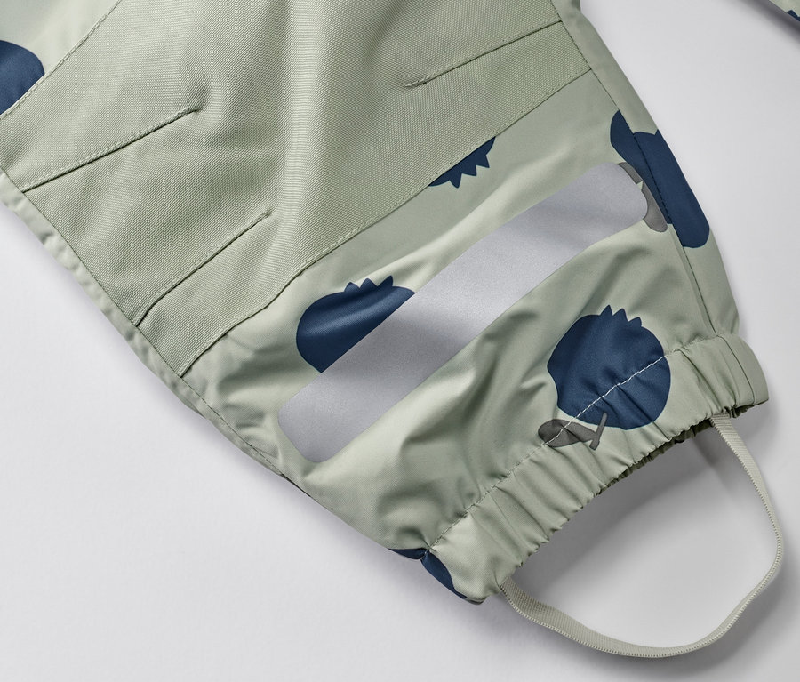 Détail d'une combinaison de pluie pour tout-petit avec un motif de myrtilles, une bande réfléchissante et un ourlet élastique.