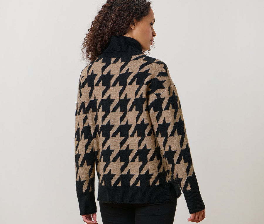 Une femme aux cheveux bouclés pose dos à la caméra et porte un pull en maille à jacquard pied-de-poule.