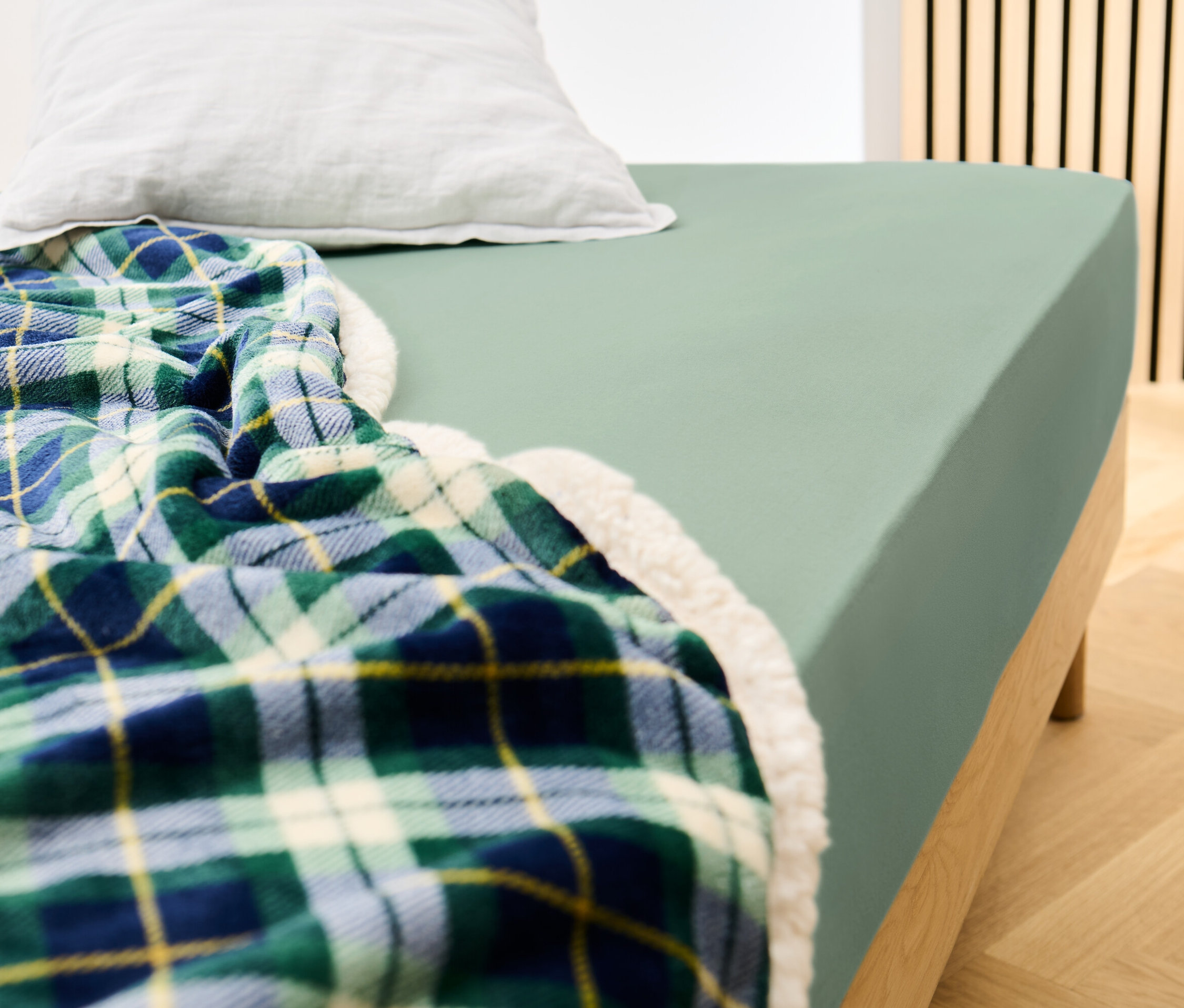 Lit avec un drap-housse en jersey vert sauge et une couverture à carreaux.