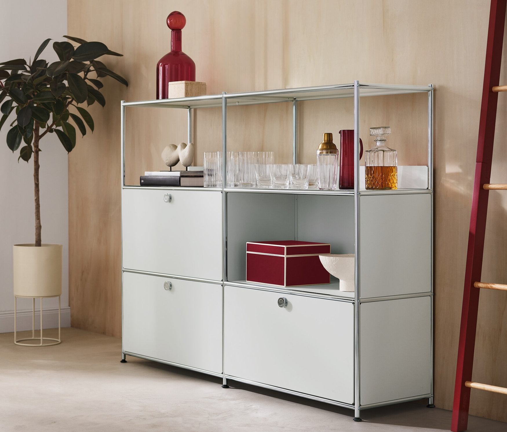 Dans la pièce, il y a un cache-pot rond avec une plante, une commode en métal « CN3 » à 2 abattants et 1 tiroir et une échelle décorative avec des éléments latéraux rouges.