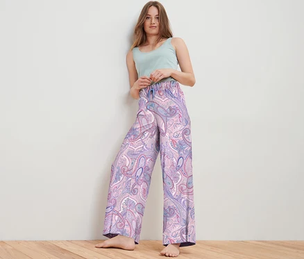 Une femme pose en studio et porte un pantalon relax tissé à motif cachemire et un haut vert clair.