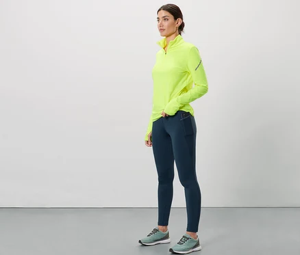 Une femme porte un legging thermique de course bleu foncé et un haut jaune néon.