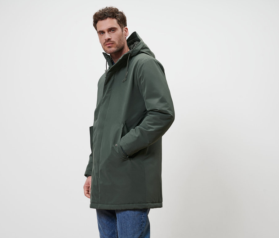 Un homme pose en parka verte et en jean.