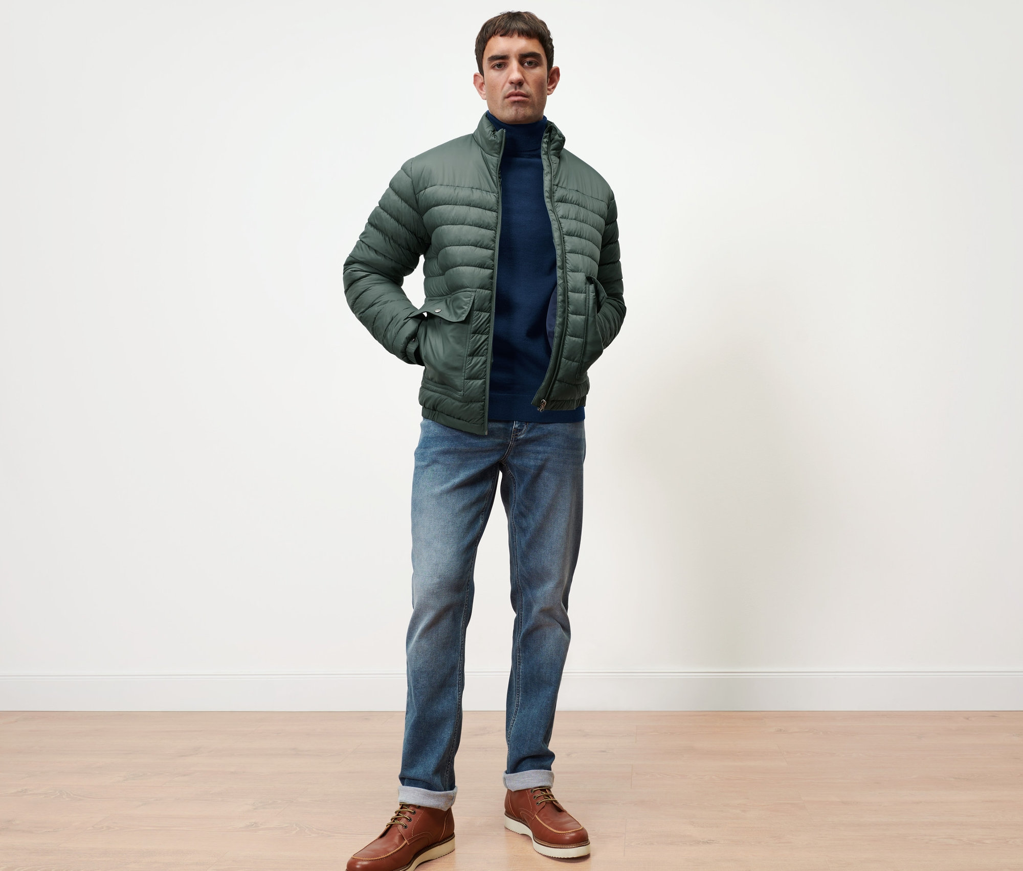 Un homme debout porte un pull en mérinos bleu marine et une veste matelassée verte.