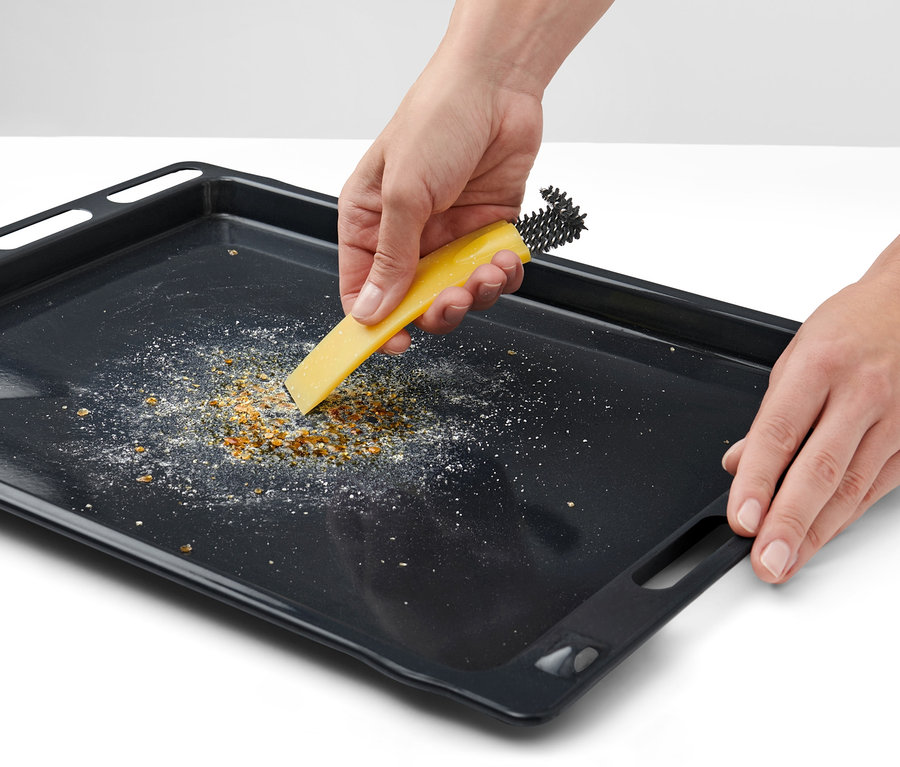 Des mains nettoient une plaque de cuisson avec une brosse à four avec racloir.
