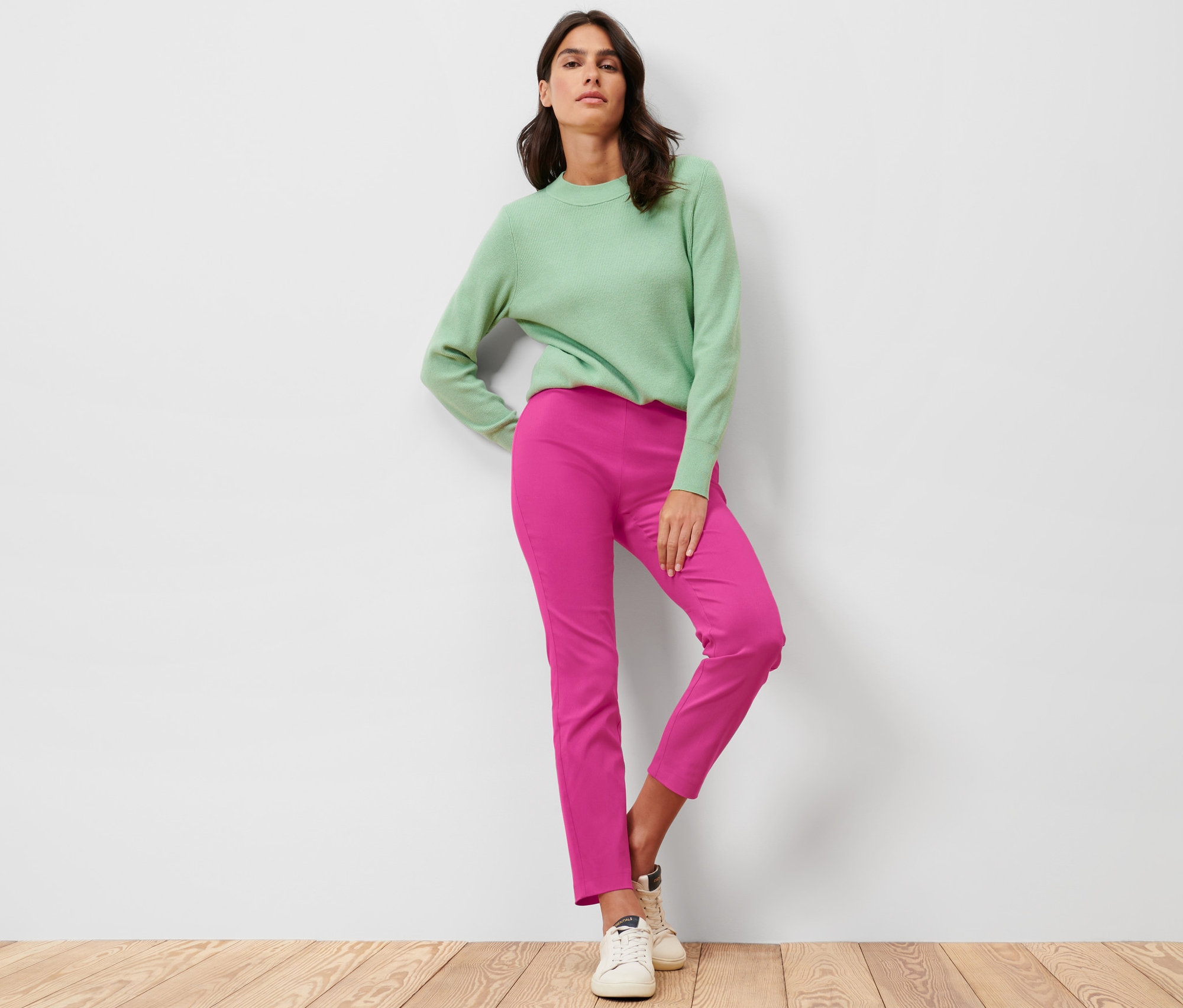 Femme posant en pull vert et pantalon stretch rose vif.