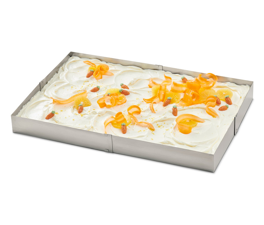 Un gâteau décoré d'écorces d'orange et de carottes dans un cadre à pâtisserie en acier inoxydable.