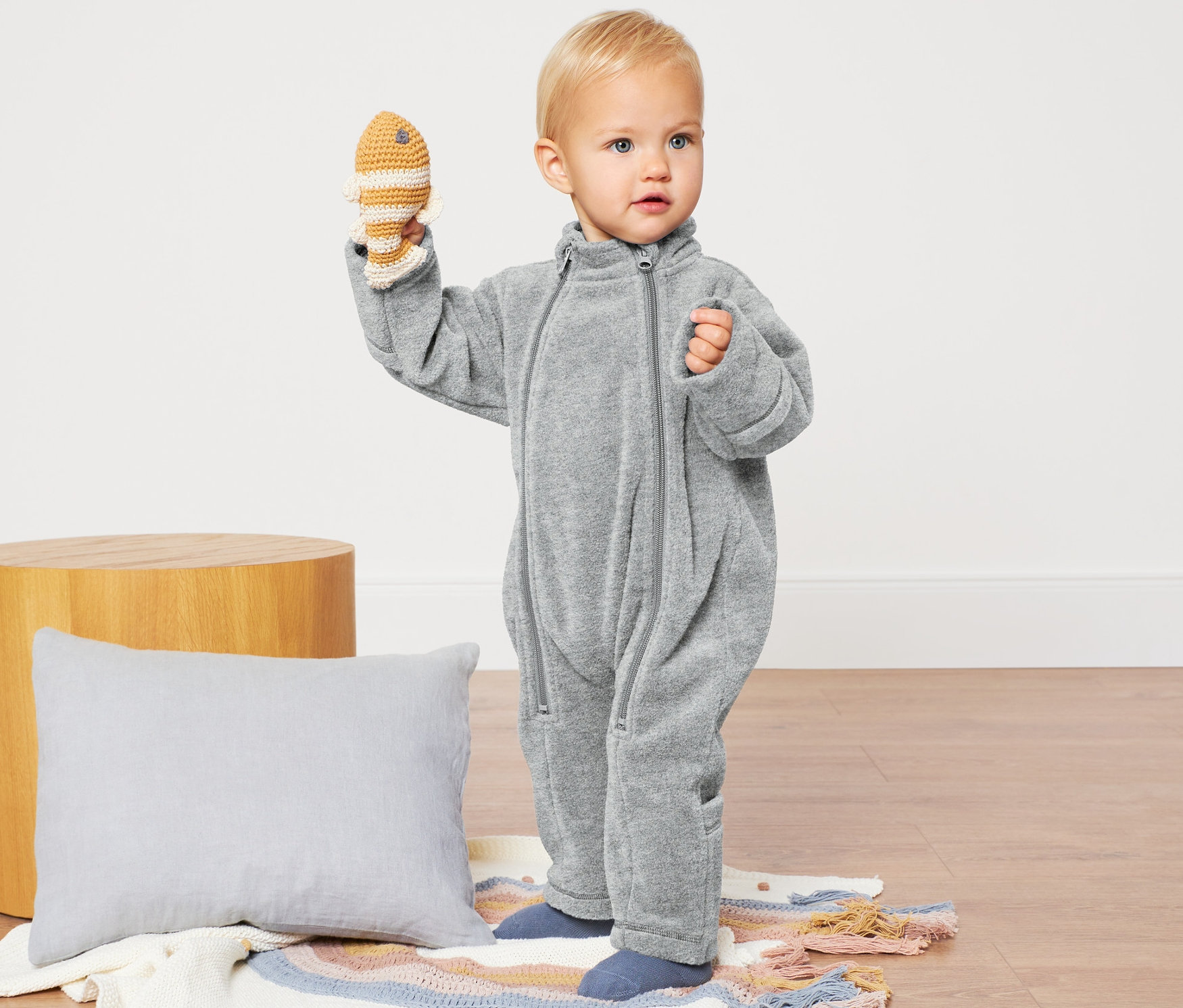 Un bébé tient un poisson au crochet et porte une combinaison en polaire grise.