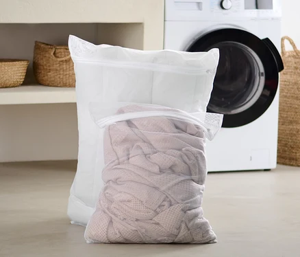 Deux grands filets à linge sont posés sur le sol de la salle de bain devant une machine à laver.