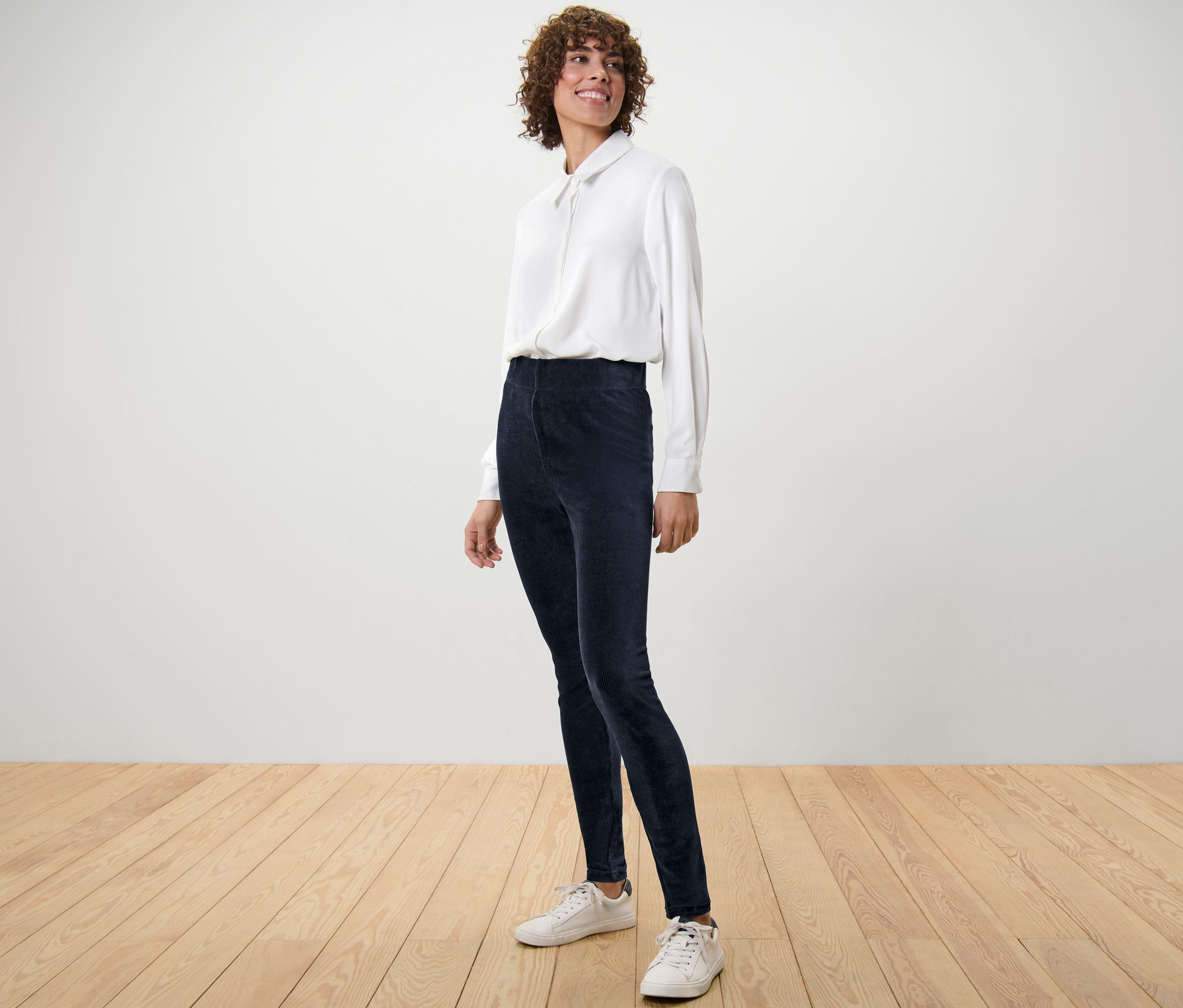 Femme posant en leggings en velours côtelé et chemise blanche.