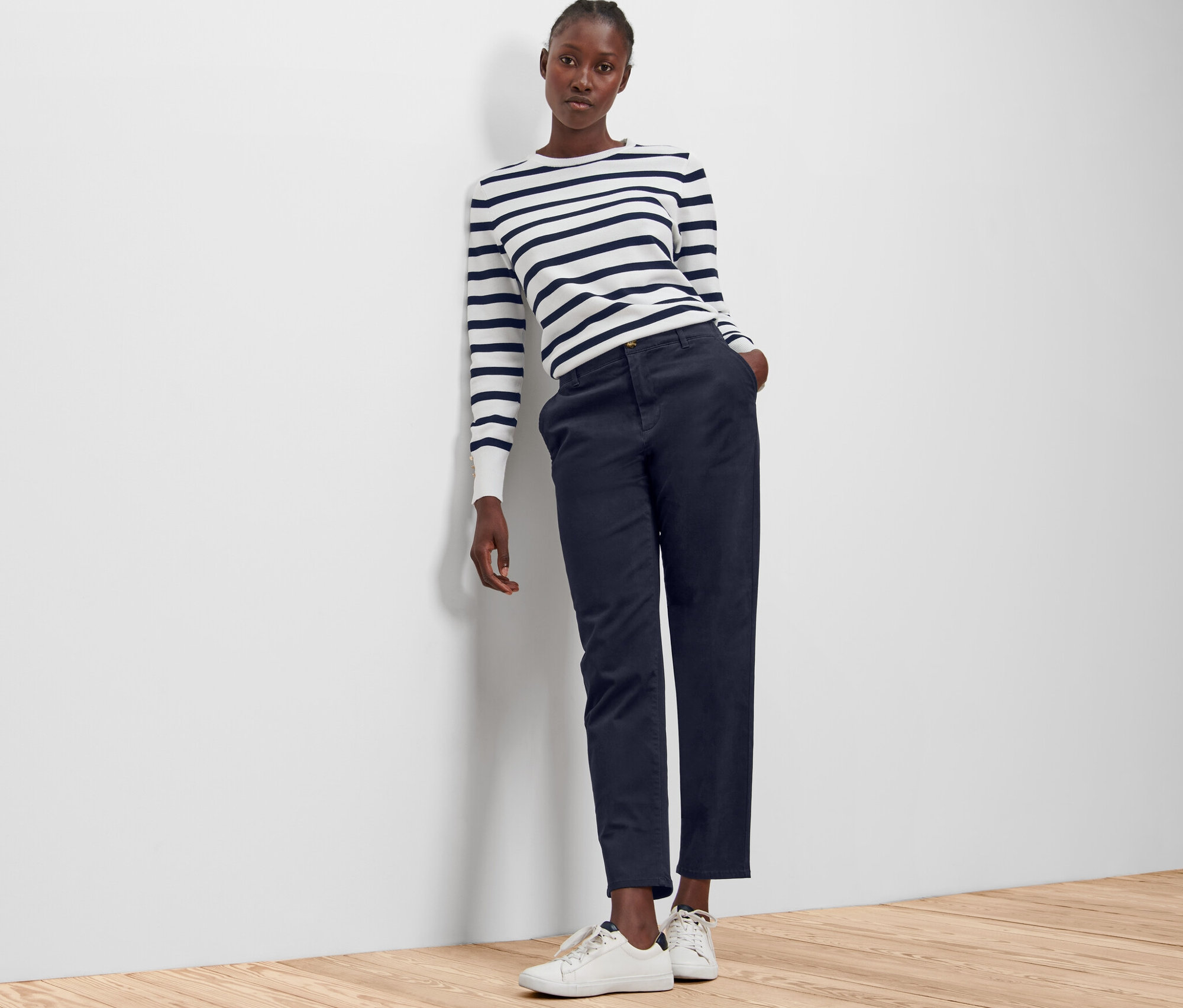 Une femme appuyée contre un mur porte un pantalon chino bleu foncé.