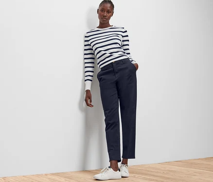 Une femme appuyée contre un mur porte un pantalon chino bleu foncé.