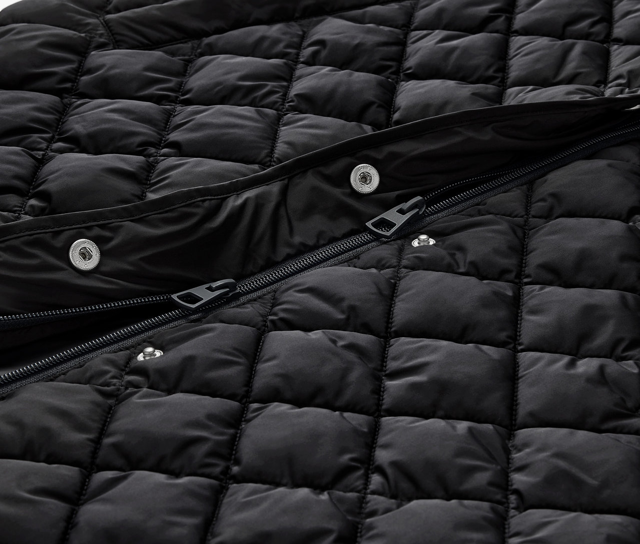 Détail d'un long gilet matelassé noir avec capuche, avec fermeture éclair et boutons-pression.