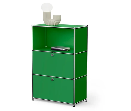 Un meuble de rangement modulaire vert avec deux portes et une étagère ouverte sur laquelle repose un livre. Une lampe est posée sur le dessus.