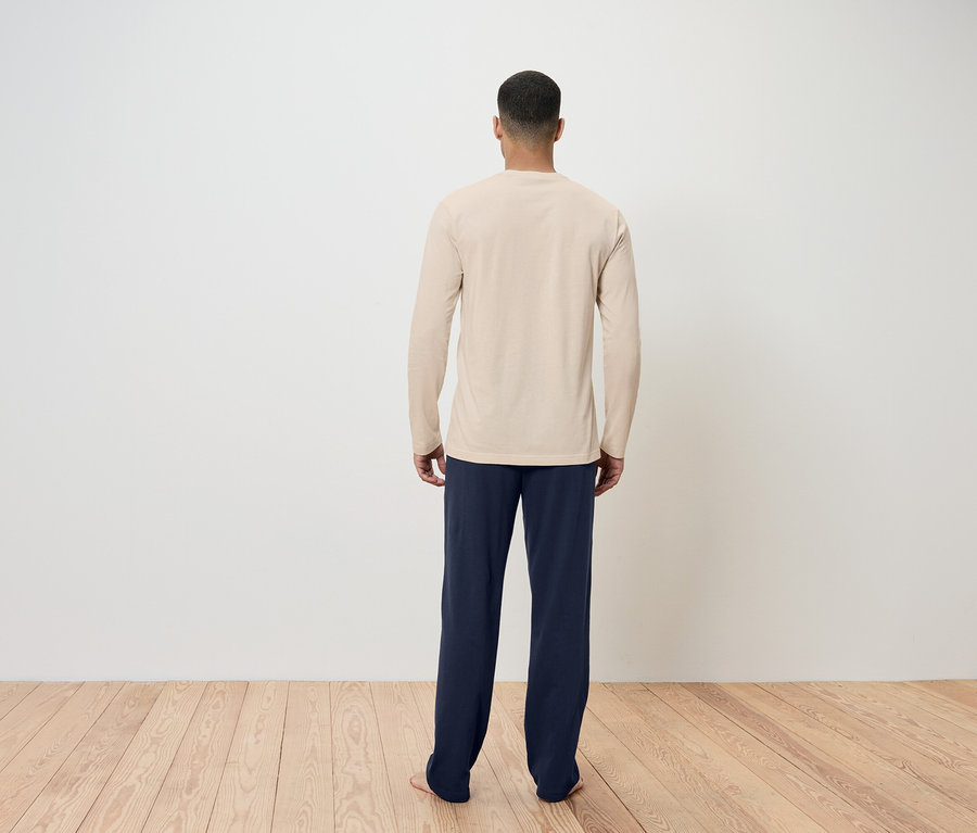 Un homme, vu de dos, porte un t-shirt beige à manches longues et un pantalon bleu marine.