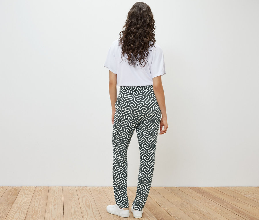 Vue arrière d'une femme portant un t-shirt blanc et un pantalon en jersey imprimé vert.