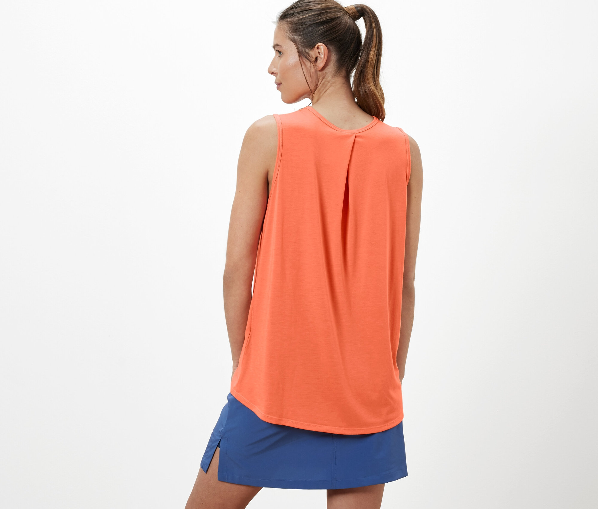 Une femme portant un haut fonctionnel orange pour l’extérieur et une jupe bleue.