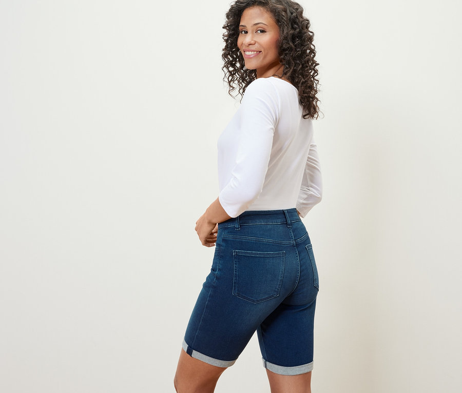 Une femme regarde par-dessus son épaule et porte un bermuda en jean coupe « Lea » en denim bleu foncé.