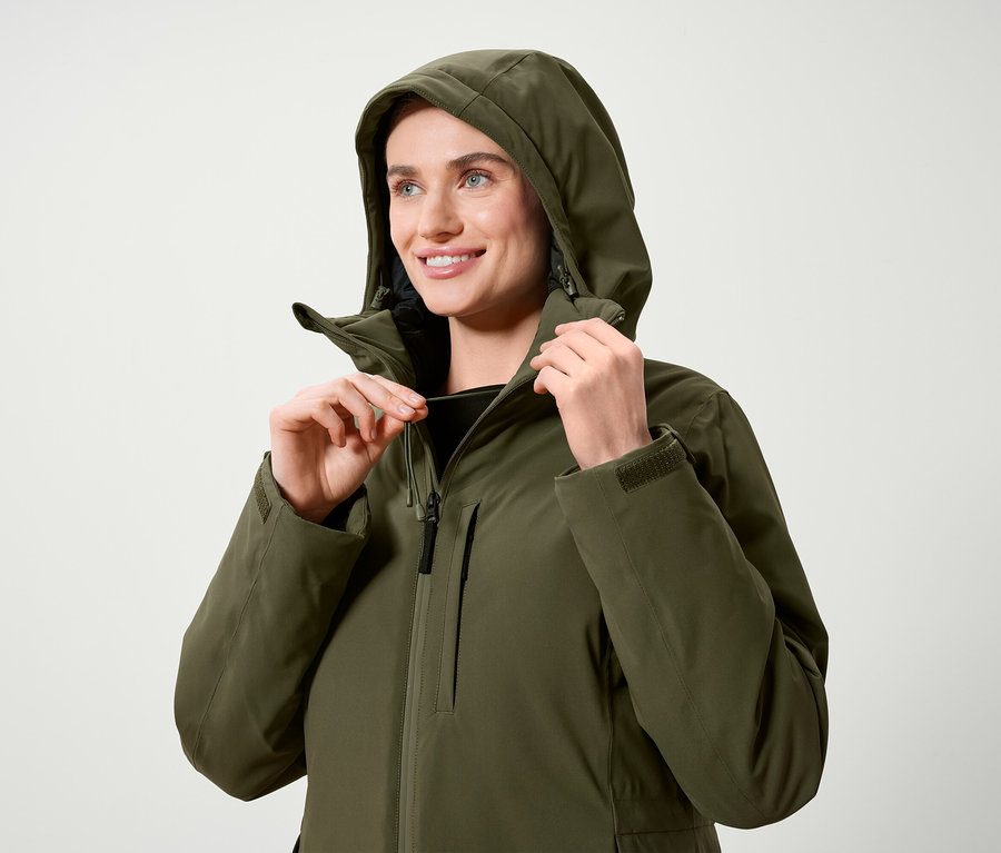 Une femme ajuste la capuche d'une veste vert olive.